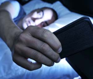 Man using his phone in bed with his face illuminated by the screen