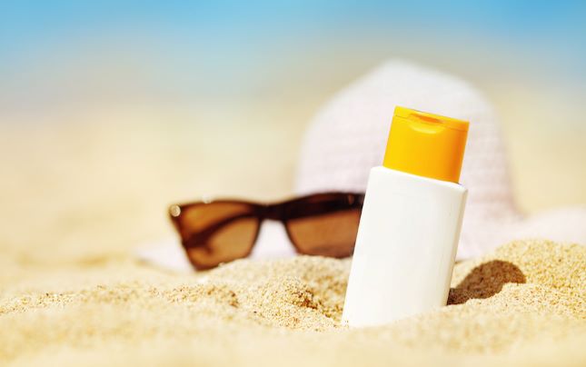Bottle of sunscreen with shades on a beach