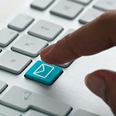 Closeup of hand hovering over computer keyboard with blue email button