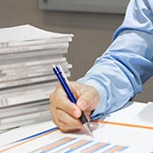 Man's hand writing on stack of papers with blue pen