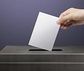 Woman's hand depositing paper ballot into nomination box