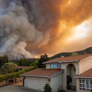 wildfire rages behind a house