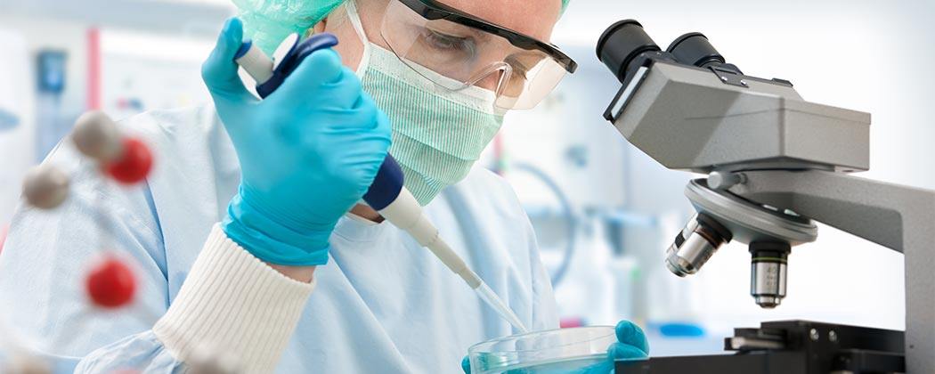 Scientist in safety gear examining a petri dish